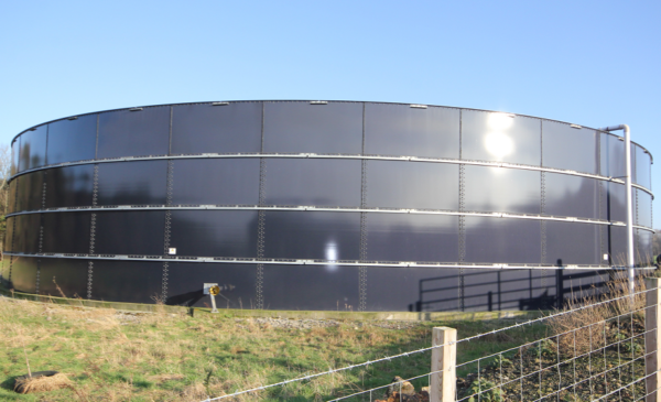 A large 4-ringed metal above ground slurry store with sunlight reflecting off the curved surface.