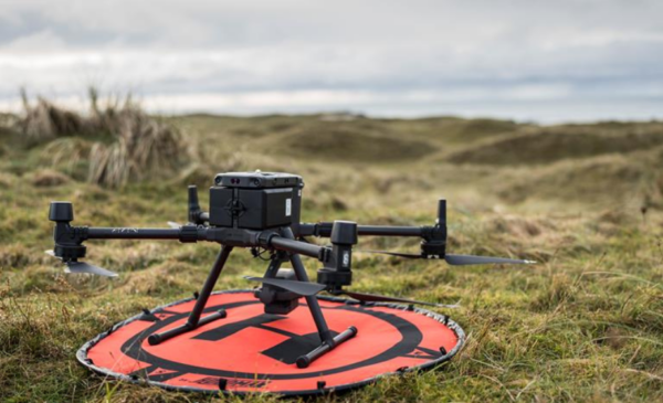 A large drone sat on a red landing pad in an upland grass pasture field.