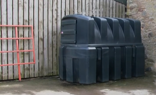 A double bunded plastic fuel tank sitting in the corner of a farmyard with a red gate nearby.